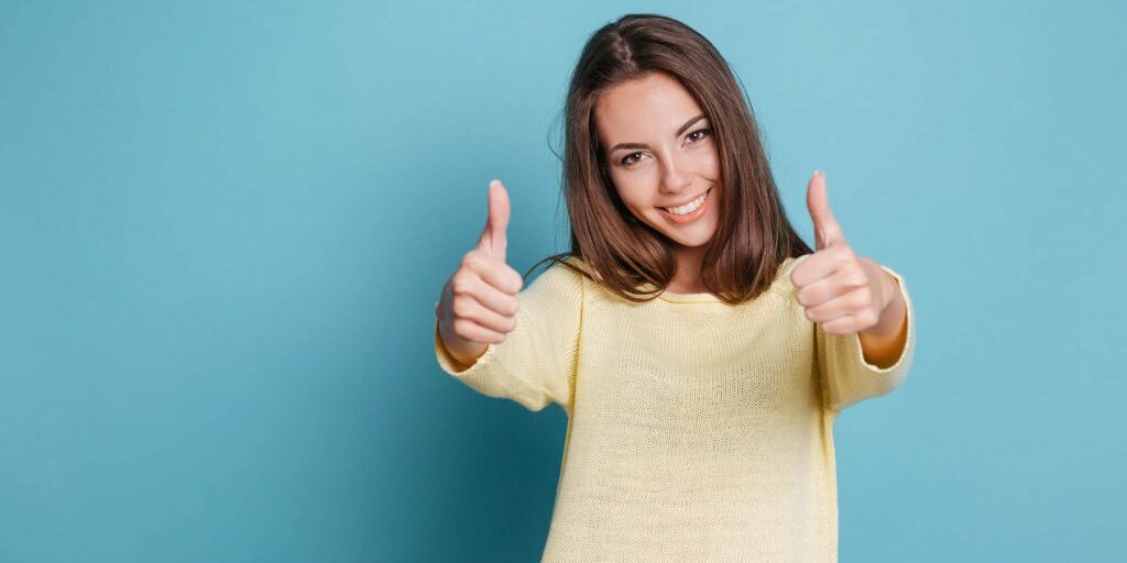 Beautiful smiling young woman giving thumbs up isolated on the blue background